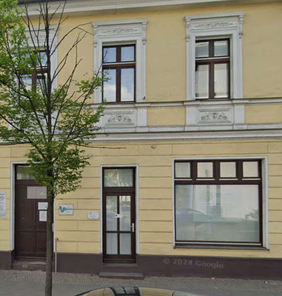 Yellow two-story building with ornate white window frames, a tree in front, and a dark doorway on a city street.
